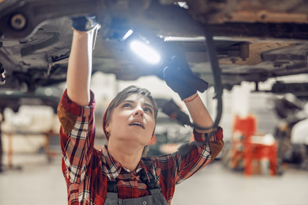 Female technician working with a flashlight under a lifted car. How to Choose the Right Mechanic