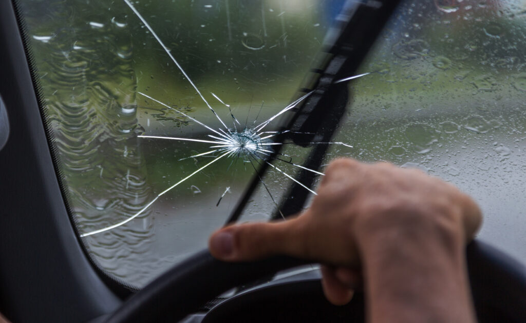 Broken windshield of a car. A web of radial splits, cracks on the triplex windshield. Broken car windshield, damaged glass with traces of oncoming stone on road or from bullet trace in car glass. Crack a Windshield